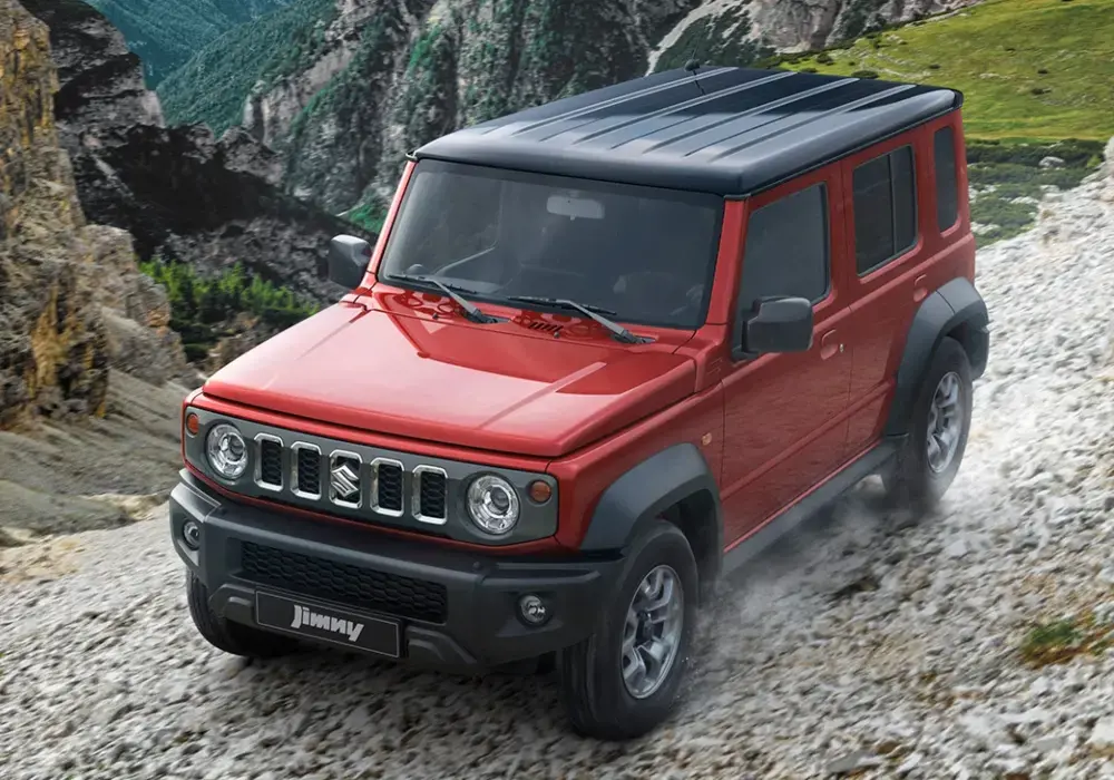 Suzuki Jimny rojo de 5 puertas, con techo negro, estacionado en una superficie rocosa.